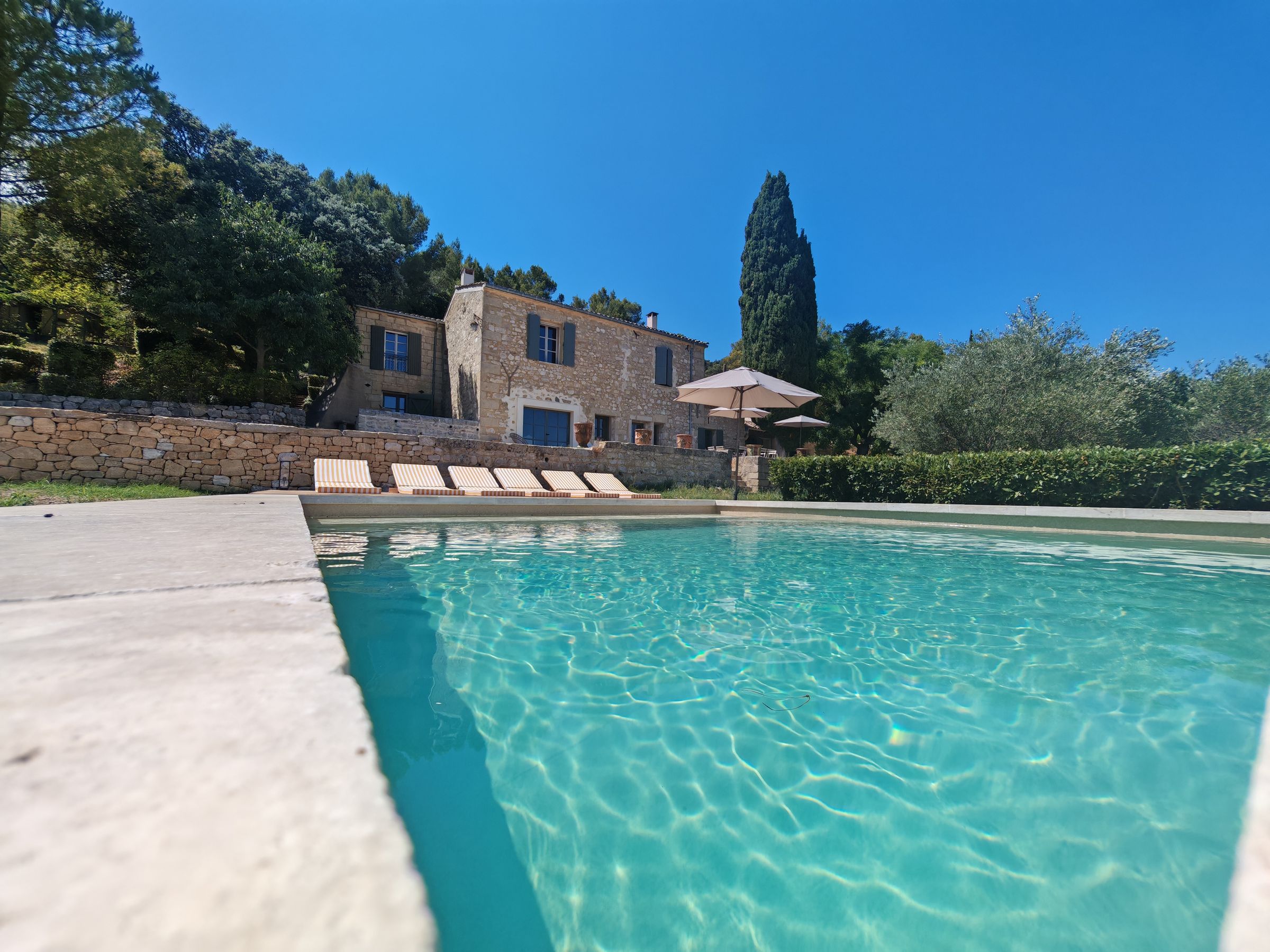 Sonnige spanische Natursteinvilla mit großem Pool, blauem Himmel und grünem Garten
